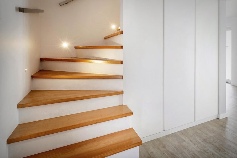 Wendeltreppe mit Holzstufen und integrierter Beleuchtung neben einem weißen Schrank.