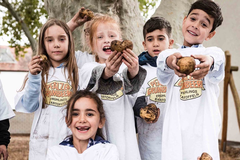 Eine Gruppe Kinder präsentiert Frühkartoffeln vor einem Baum.