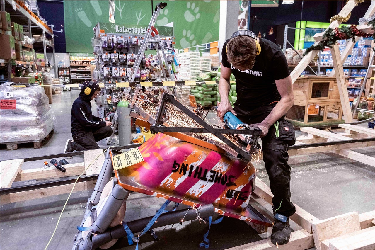 Ein Mann in Arbeitskleidung benutzt einen Winkelschleifer an einer Metallkonstruktion in einem Baumarkt.