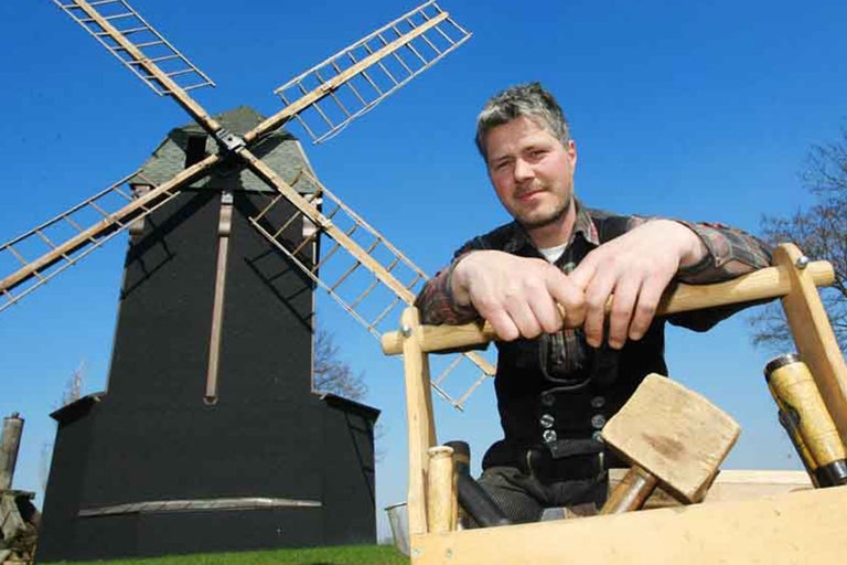 Zimmermann in traditioneller Arbeitskleidung mit Windmühle im Hintergrund