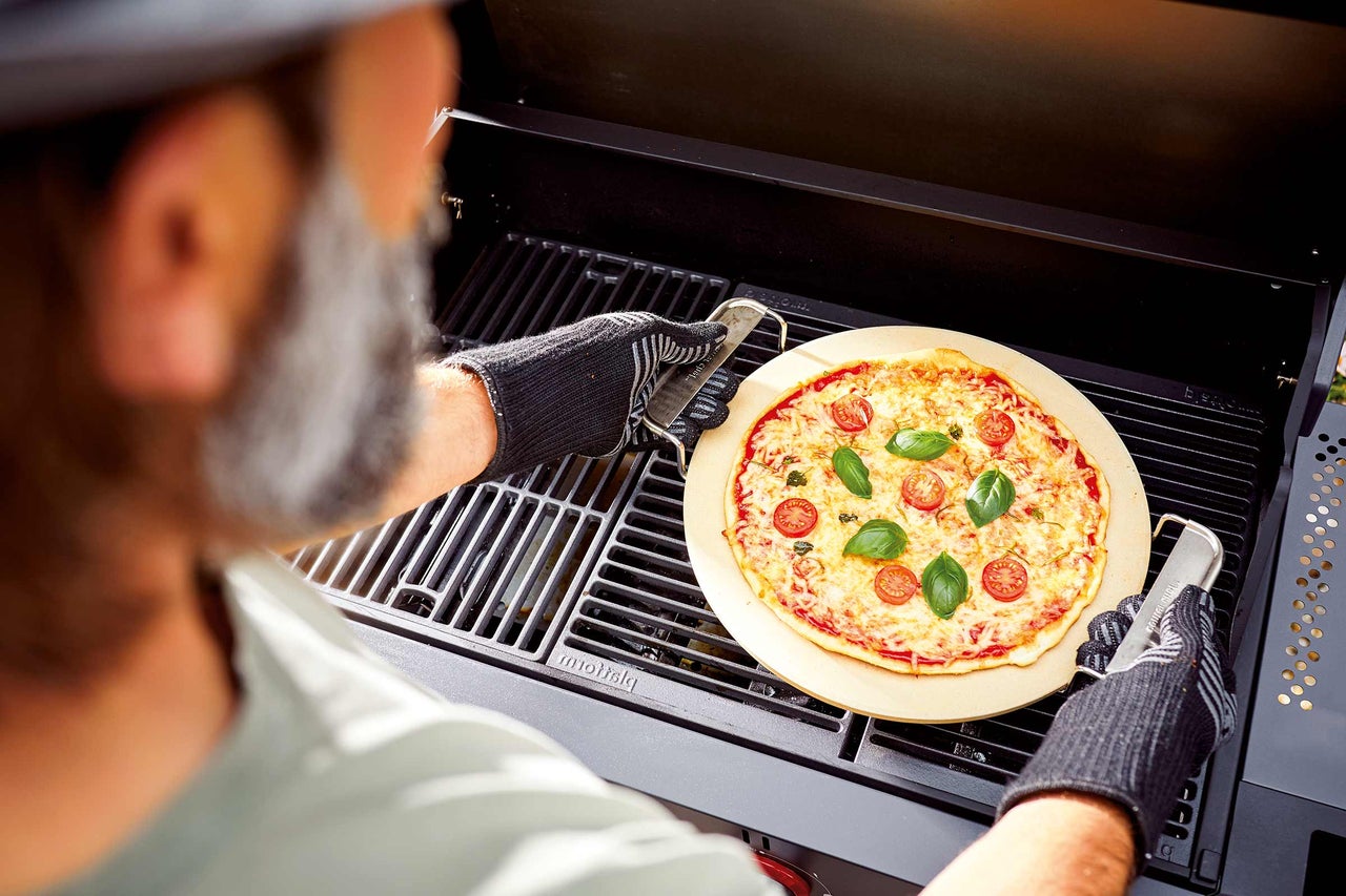 Eine Person legt eine Pizza auf einem Pizzastein in einen Grill.