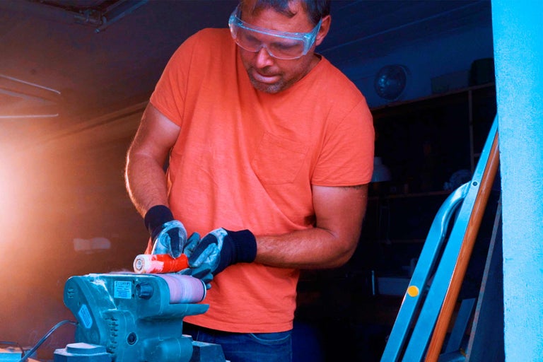 Mann schleift Werkstück mit einer Bandschleifmaschine in einer Werkstatt