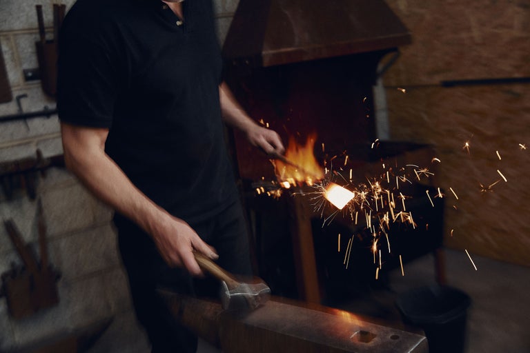 Schmied bearbeitet glühendes Metall mit Hammer am Amboss in der Schmiede