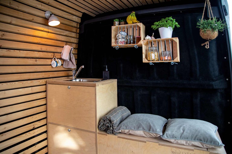 Innenraum eines Wohnmobils mit Holzwand, Waschbeckenunterschrank, Regalen und Dekoration