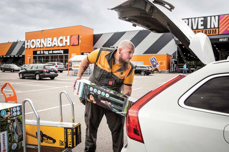Ein Mann lädt Gartengeräte von Gardena und Dewalt in den Kofferraum eines Autos auf dem Parkplatz von Hornbach.