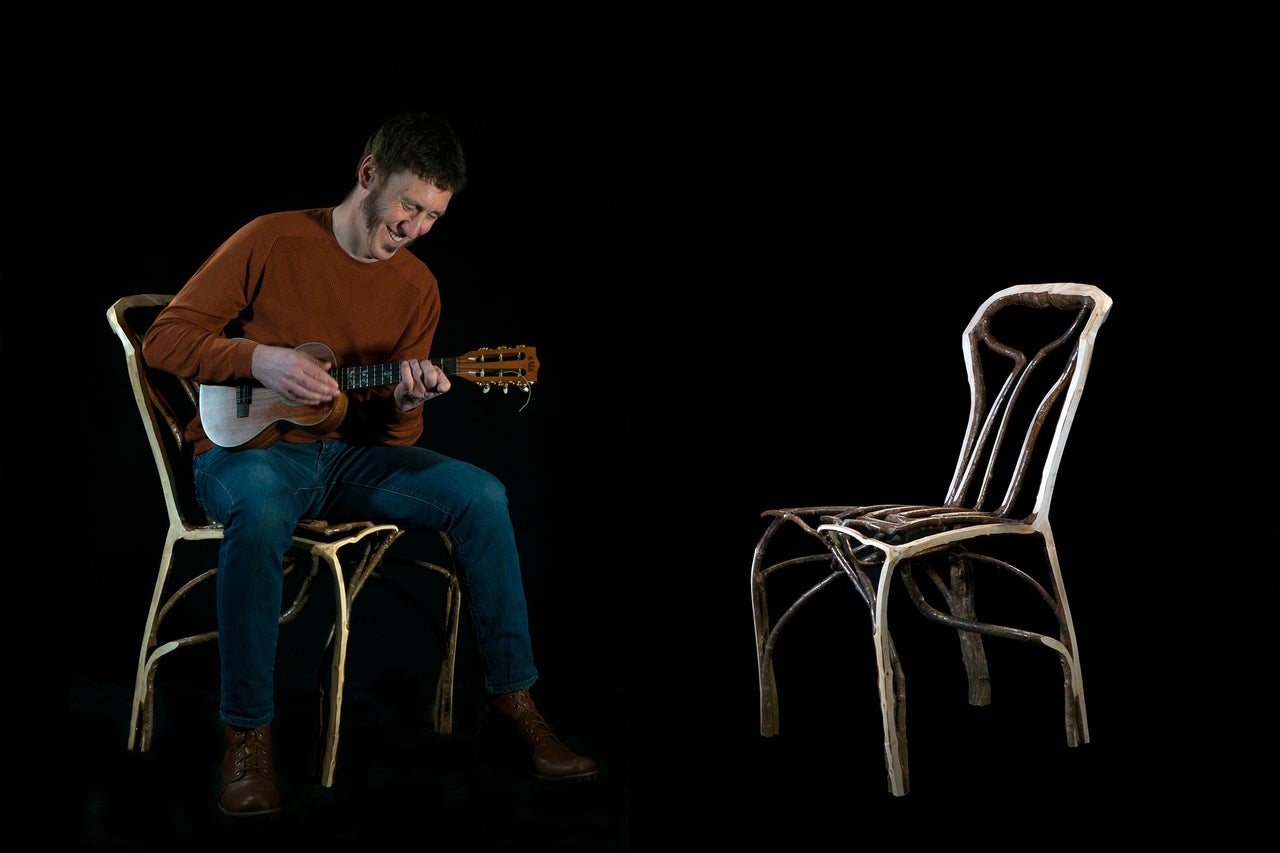 Mann sitzt auf einem Stuhl und spielt Ukulele, daneben steht ein leerer Stuhl