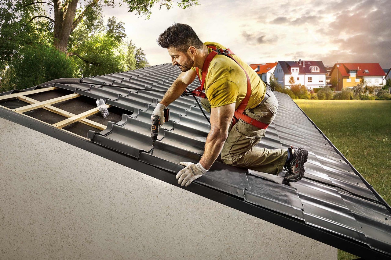 Ein Handwerker befestigt Dachziegel mit einem Akkuschrauber auf einem Dach.