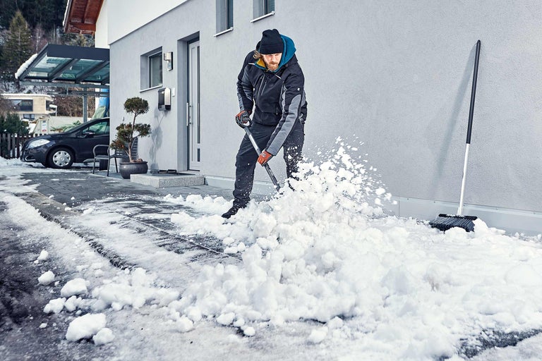 Mann schaufelt Schnee vor Haus mit Schneeschaufel