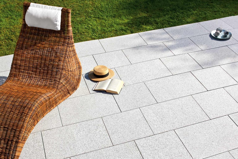 Gartenszene mit Rattanliege, Pflastersteinen und Sommeraccessoires