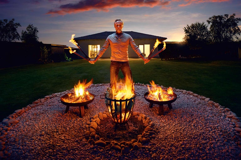 Mann mit Fackeln und Feuerschalen im Garten bei Dämmerung