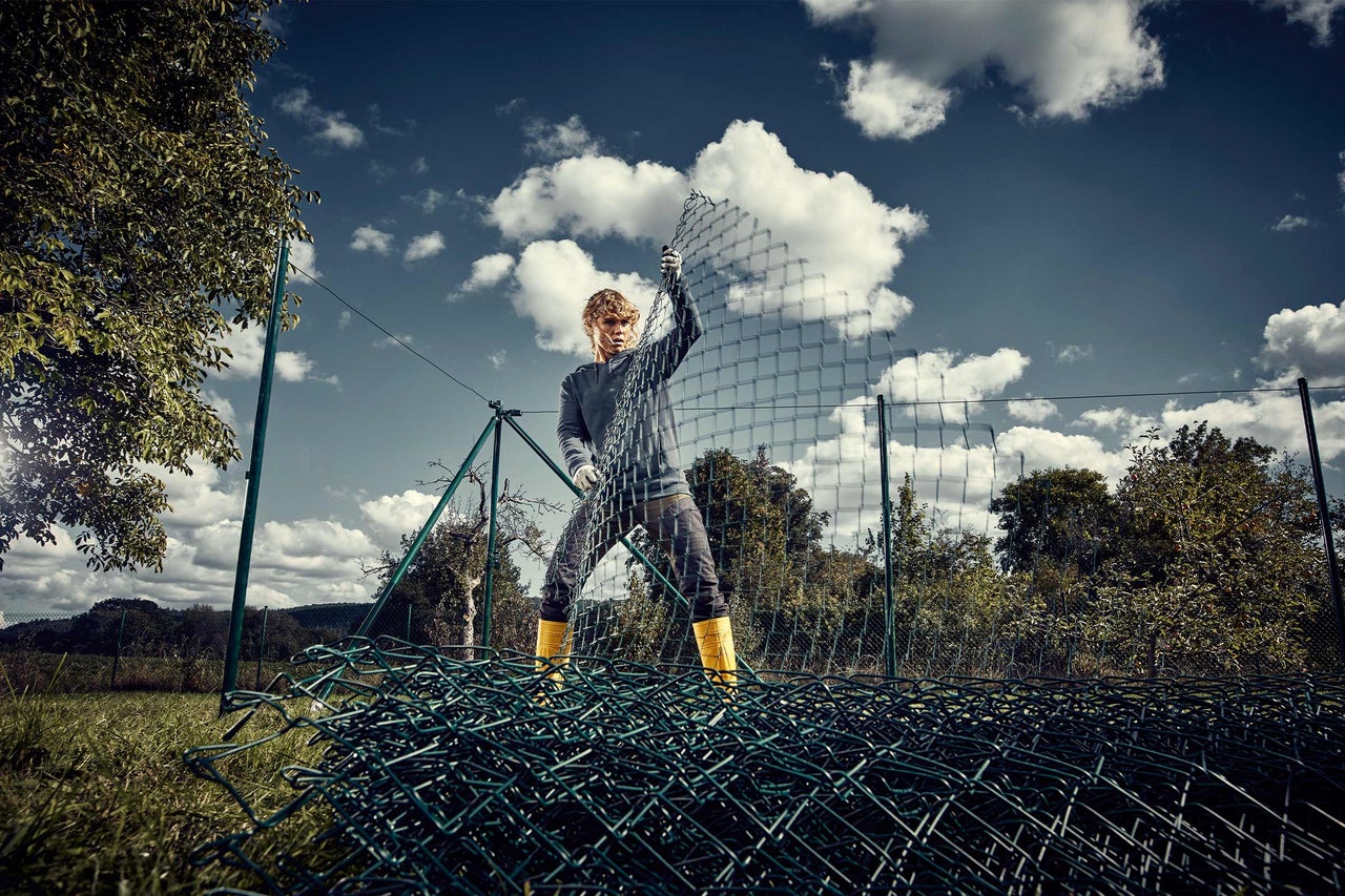 Ein Mann installiert einen Rollenzaun im Garten, der als Grundstücksbegrenzung dient.