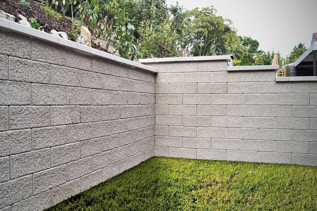 Eine aus Betonsteinen errichtete Gartenmauer mit Rasenfläche im Vordergrund.