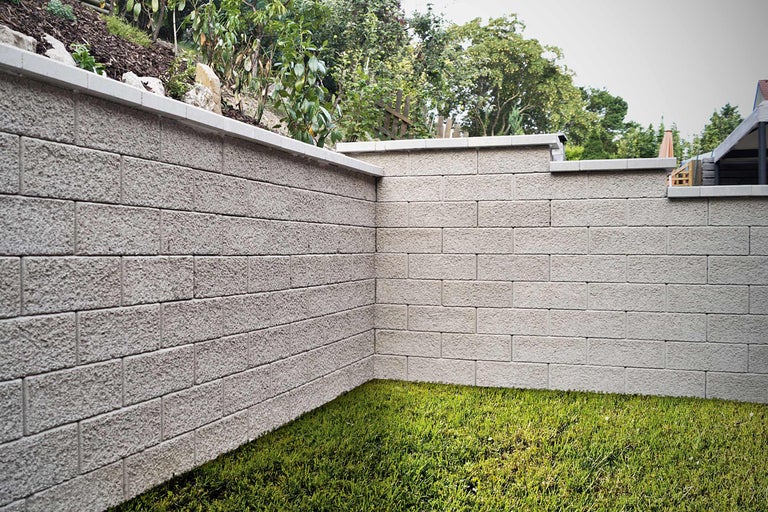 Eine aus Betonsteinen errichtete Gartenmauer mit Rasenfläche im Vordergrund.