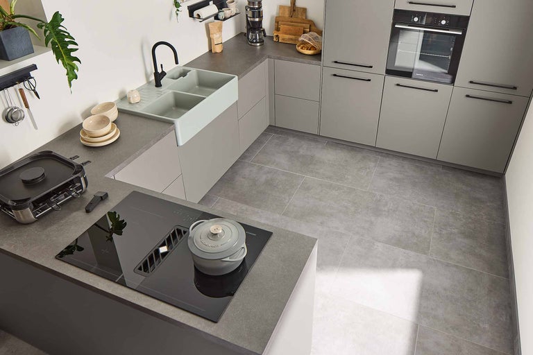 Helle Küche mit Küchenspüle, Kochfeld, Dunstabzugshaube, Backofen und Küchenutensilien.