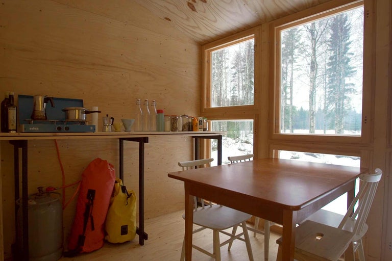 Innenansicht eines Raumes mit Tisch, Stühlen und Regalen vor dem Fenster.