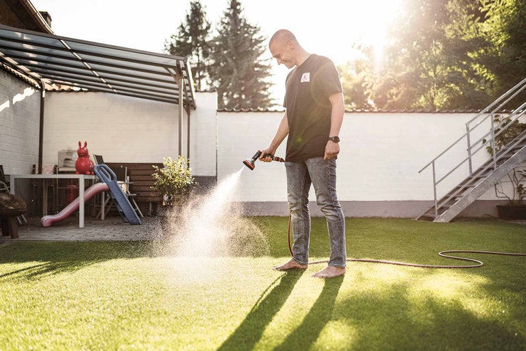 Mann bewässert Rasen mit einem Gartenschlauch im Garten.
