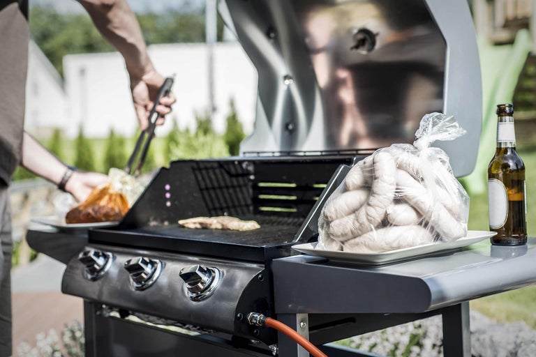 Grillszene mit Grill, Würstchen und Person mit Grillzange