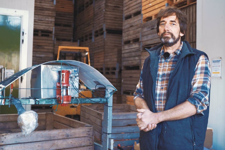 Ein Mann steht vor einem Lager mit Holzkisten und einer Maschine für die Landwirtschaft.