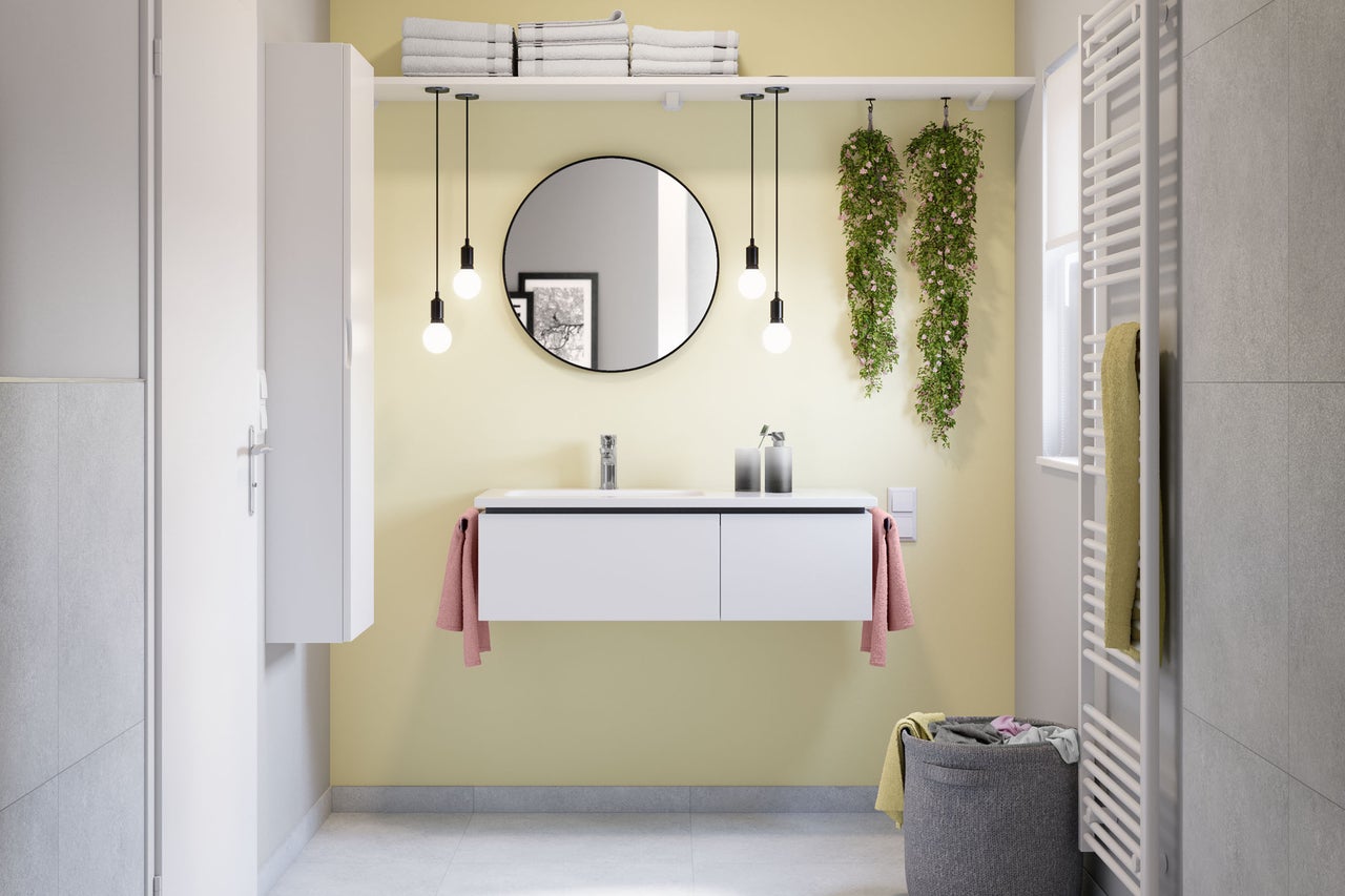 Helles, modernes Badezimmer mit weißem Waschtischunterschrank, rundem Wandspiegel, vier Pendelleuchten, Badhochschrank und Handtuchheizkörper.