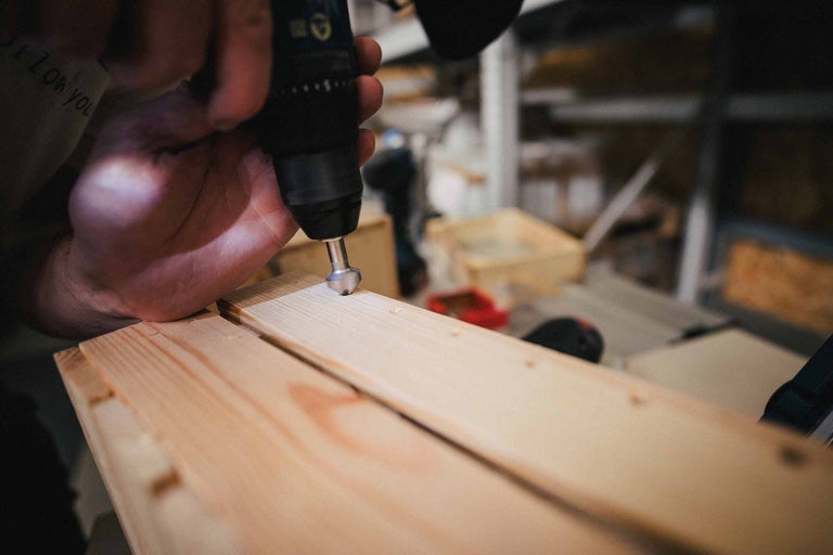 Eine Person verwendet einen Bohrer, um ein Loch in ein Holzbrett zu bohren.