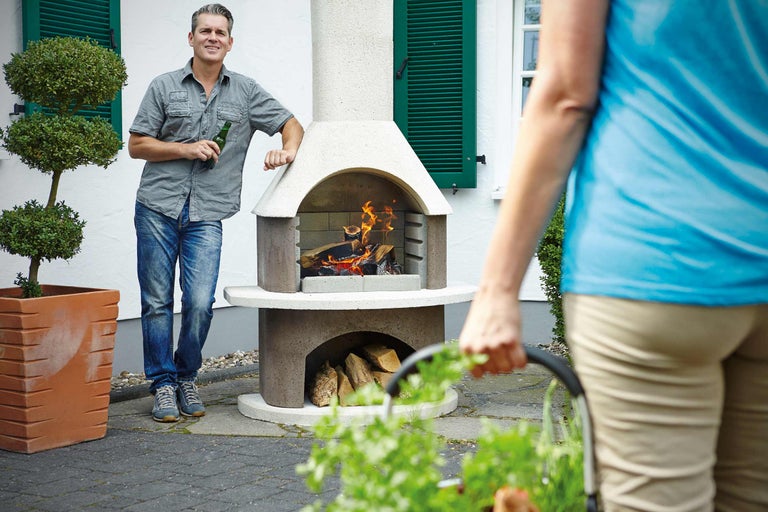 Gartenszene mit gemauertem Grillkamin, Holz, Feuer und zwei Personen