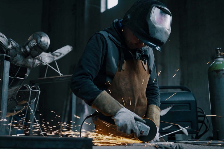 Mann mit Schutzhelm und Schürze verwendet Winkelschleifer in Werkstatt