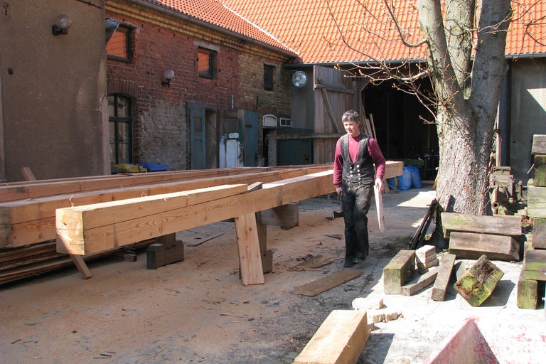 Mann im Zimmermannsoutfit arbeitet mit Holzbalken im Freien