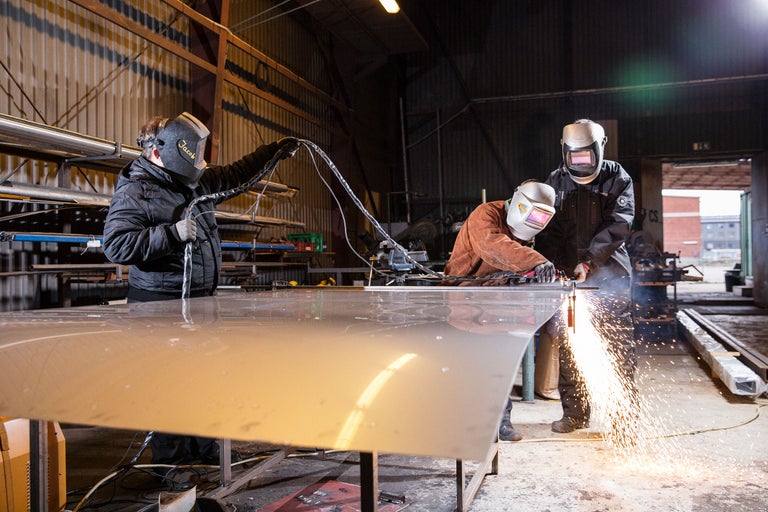 Drei Personen beim Schweißen von Metall in einer Werkstatt mit Schweißhelmen