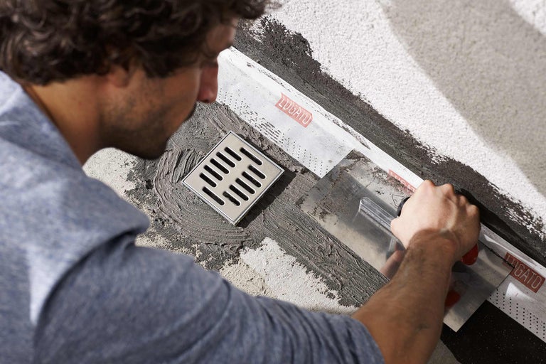 Handwerker installiert einen Bodenablauf mit Dichtmanschette und Spachtel