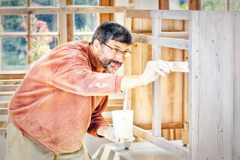 Ein Mann streicht einen Holzschrank mit einem Pinsel.