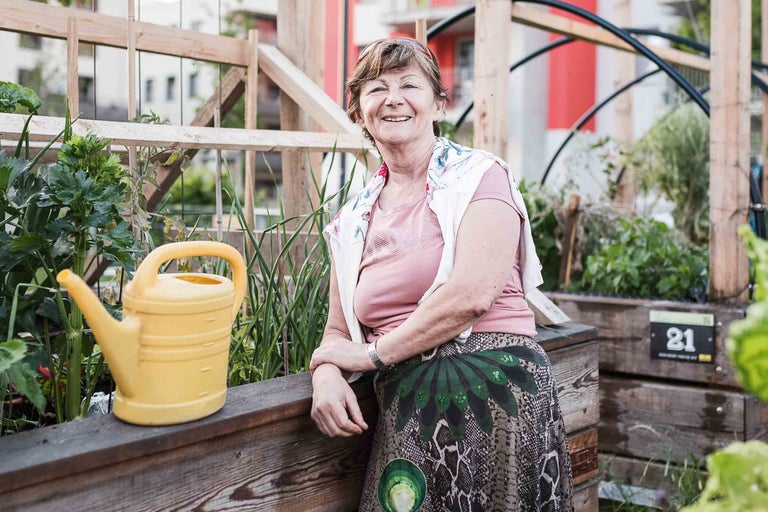 Frau in einem urbanen Garten mit Hochbeet und gelber Gießkanne