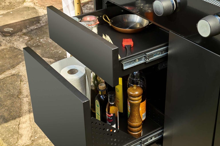 Offene Schubladen eines Grillschranks mit Kochutensilien und Zutaten