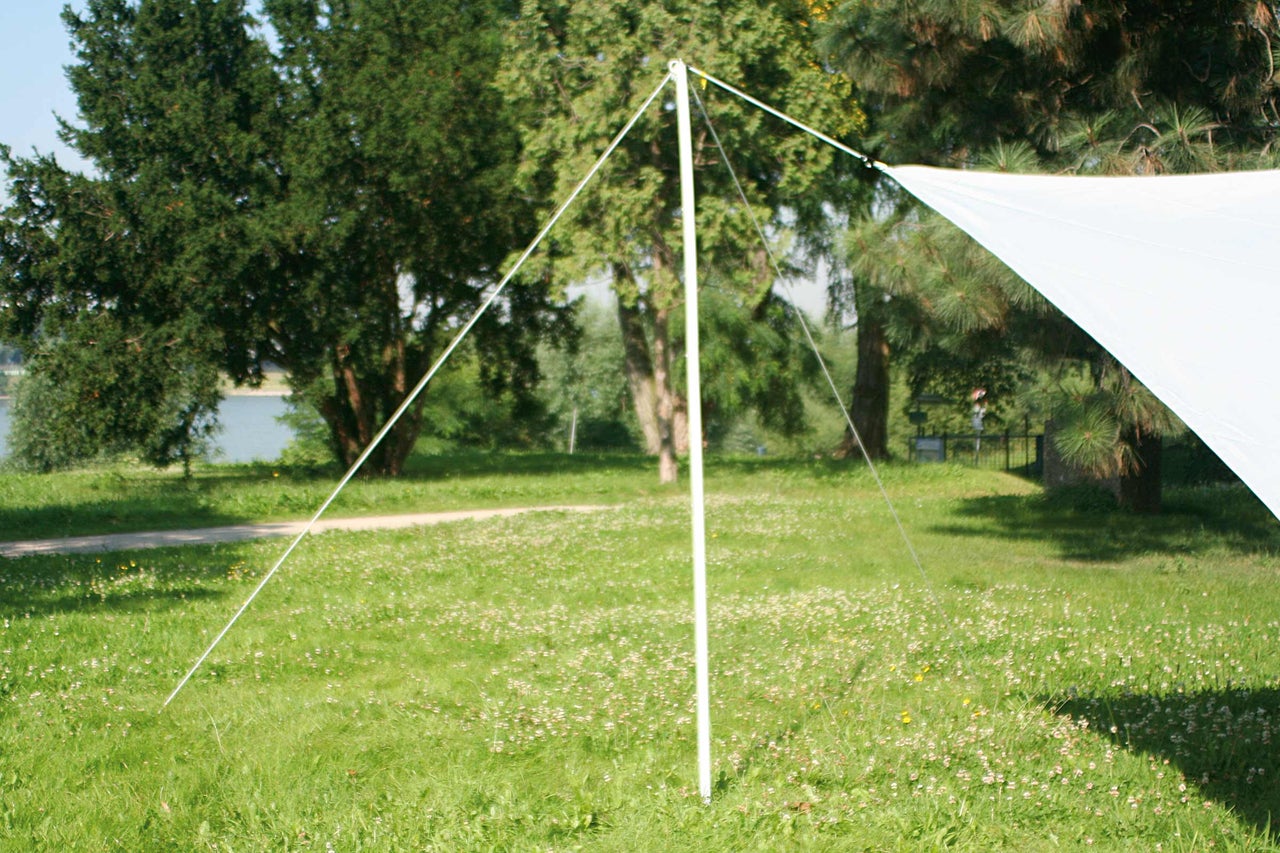 Weißes Sonnensegel auf einer Wiese, befestigt mit Seilen und einer Stange