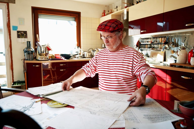 Mann in Küche betrachtet Baupläne auf Tisch.