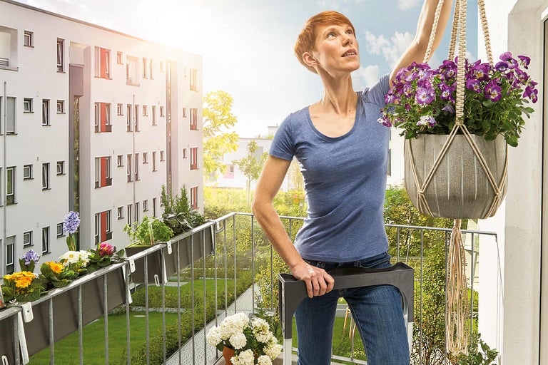 Frau schmückt Balkon mit Blumenampel und Balkonkasten.