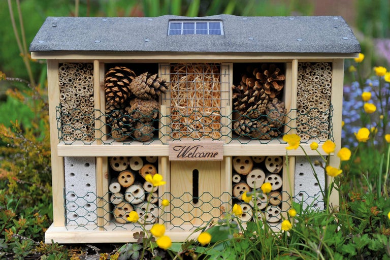 Insektenhotel aus Holz mit verschiedenen Füllmaterialien und Solarpanel auf dem Dach