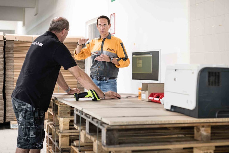 Zwei Mitarbeiter bei der Arbeit mit einem Barcode-Scanner und einem Computer auf einem Holztisch