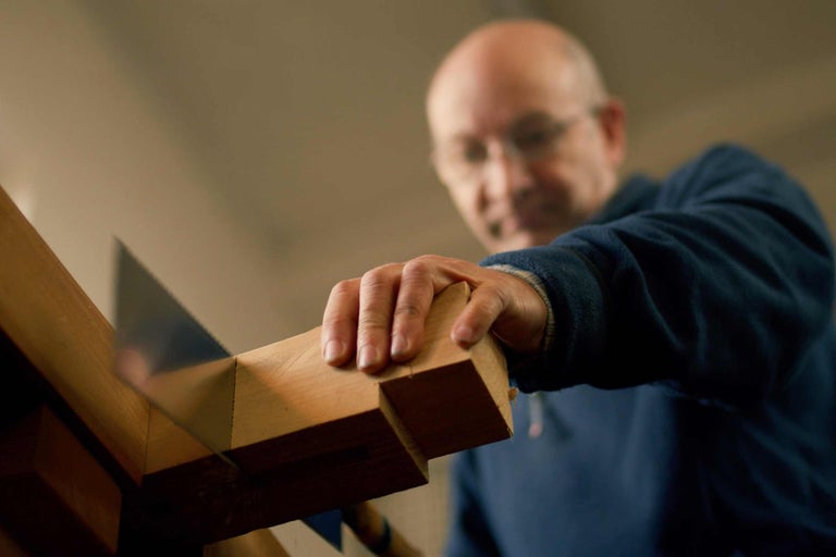 Mann sägt Holz mit einer Säge und einer Schneidlade