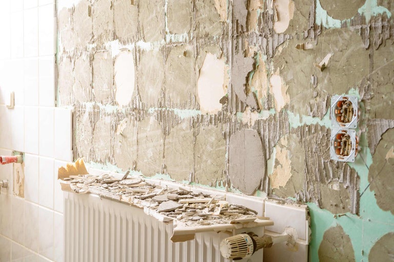 Badezimmerszene mit beschädigten Fliesen, freigelegter Wand und Heizkörper