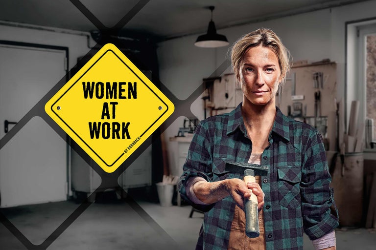 Frau mit Hammer, im Hintergrund Werkstatt und ein Schild mit der Aufschrift Women at Work von Hornbach