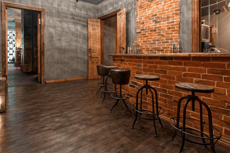Bar mit Tresen aus Ziegelsteinen und Barhockern in einem Raum mit Holzboden