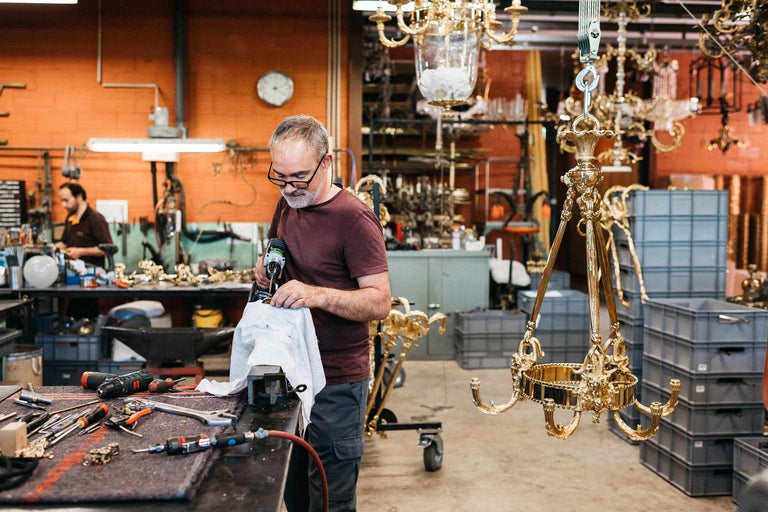 Mann arbeitet an einem goldenen Kronleuchter in einer Werkstatt mit Werkzeugen.