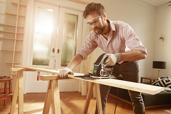 Mann sägt Holzbrett mit einer Handkreissäge auf einer Werkbank.