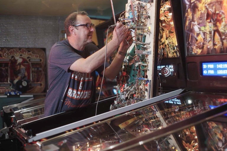 Ein Mann repariert einen Flipperautomaten.