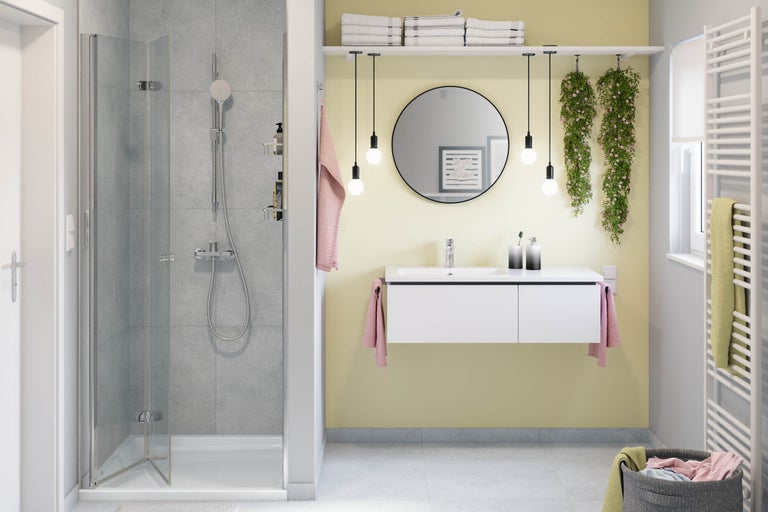 Modernes, helles Badezimmer mit Glasdusche, weißem Hängewaschtisch, rundem Spiegel, vier Pendelleuchten und einem Handtuchheizkörper.