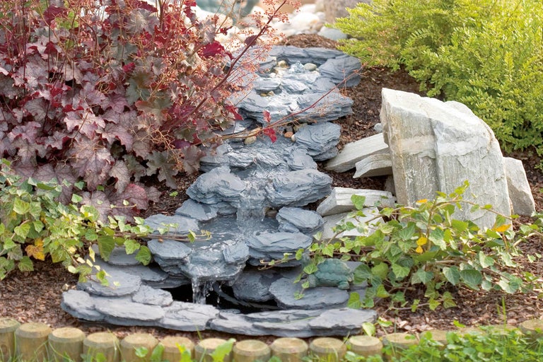 Dekorative Gartenlandschaft mit Bachlauf aus Schiefer und umgebenden Pflanzen.