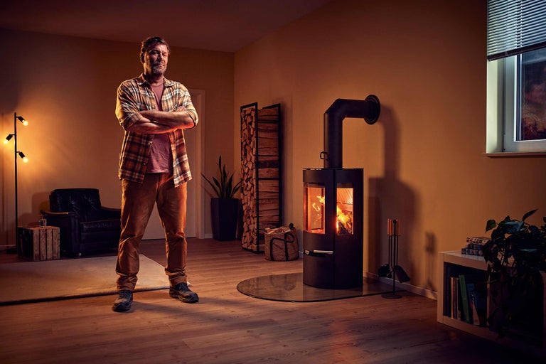 Wohnraum mit Kaminofen, Holzregal und Mann