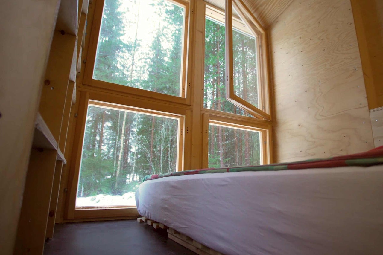Innenansicht eines Raumes mit Bett und Holzfenstern mit Blick auf Bäume.