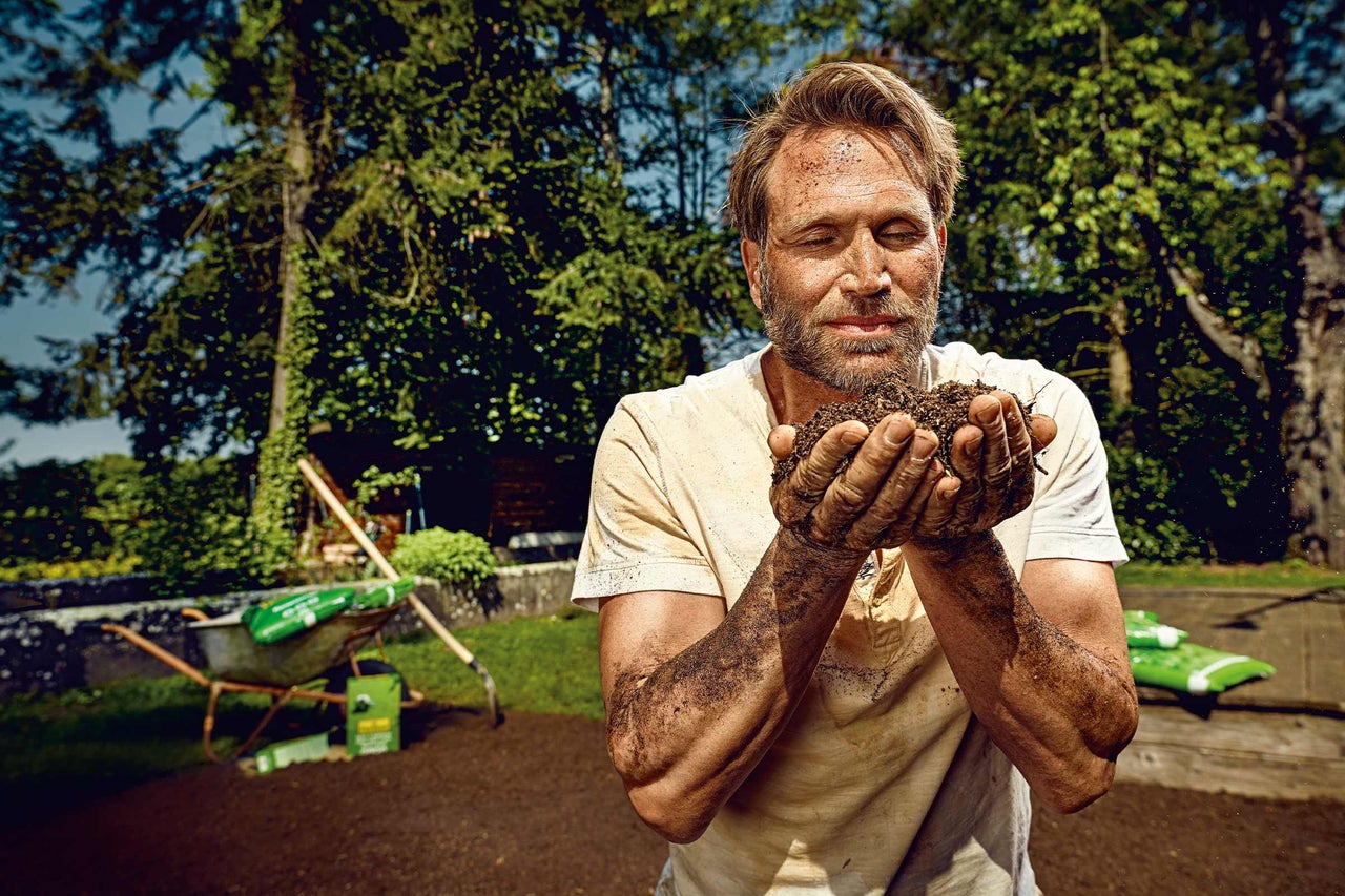 Ein Mann hält Erde in seinen Händen in einem Garten mit Gartengeräten