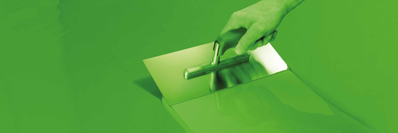 Eine Hand hält eine Glättkelle auf einem Untergrund.